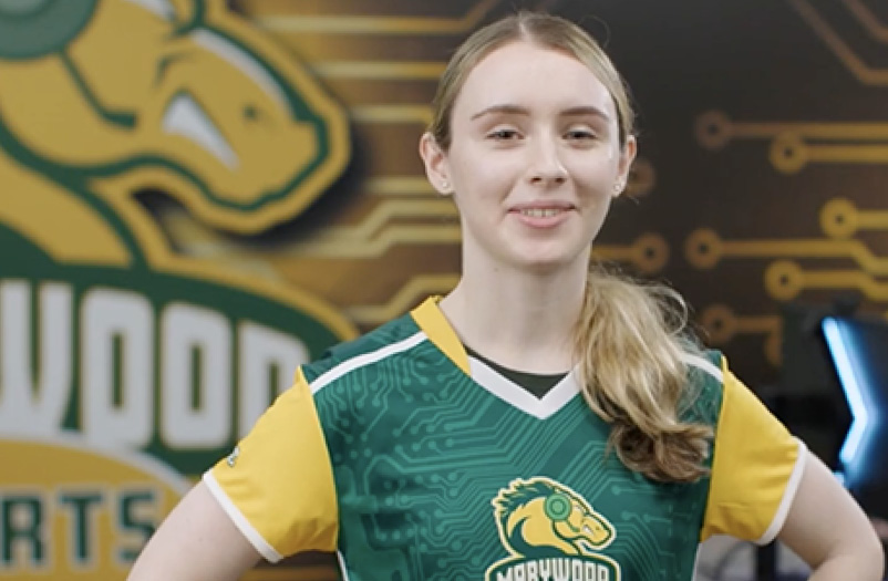 Smiling woman in a green and yellow Marywood University sports jersey posing in front of a matching team banner.